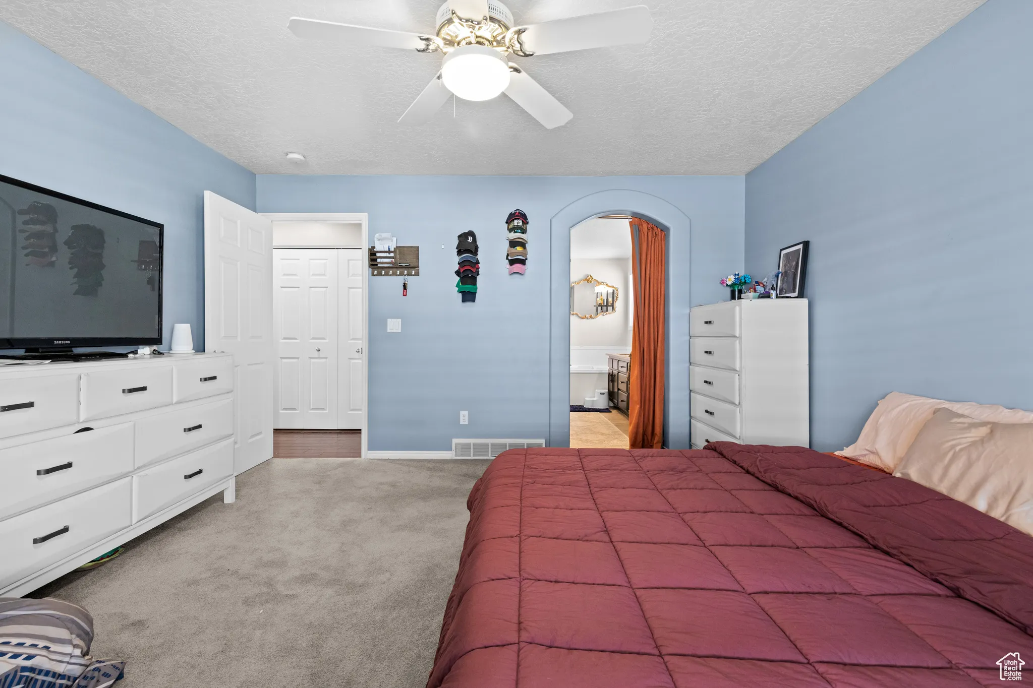 Bedroom featuring light carpet, a textured ceiling, arched walkways, ceiling fan, and ensuite bathroom