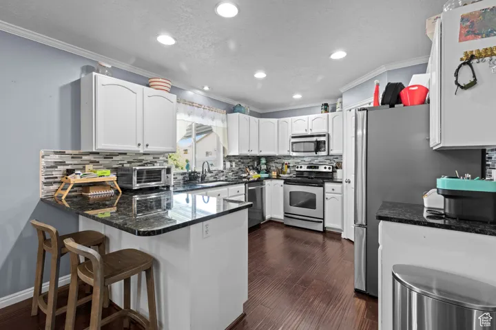 Kitchen with ornamental molding, a peninsula, a textured ceiling, white cabinets, and dark stone countertops