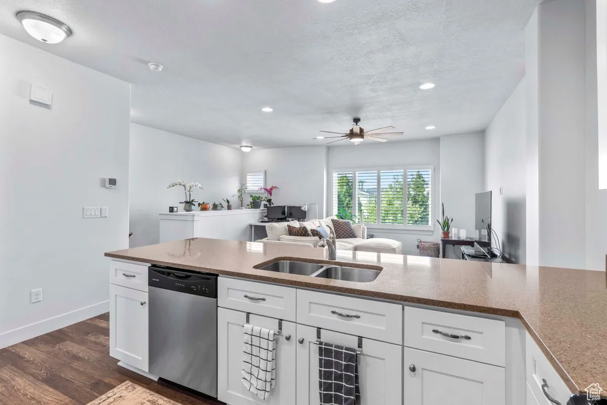 Kitchen featuring light stone counters, stainless steel dishwasher, white cabinets, dark wood-style floors, and open floor plan