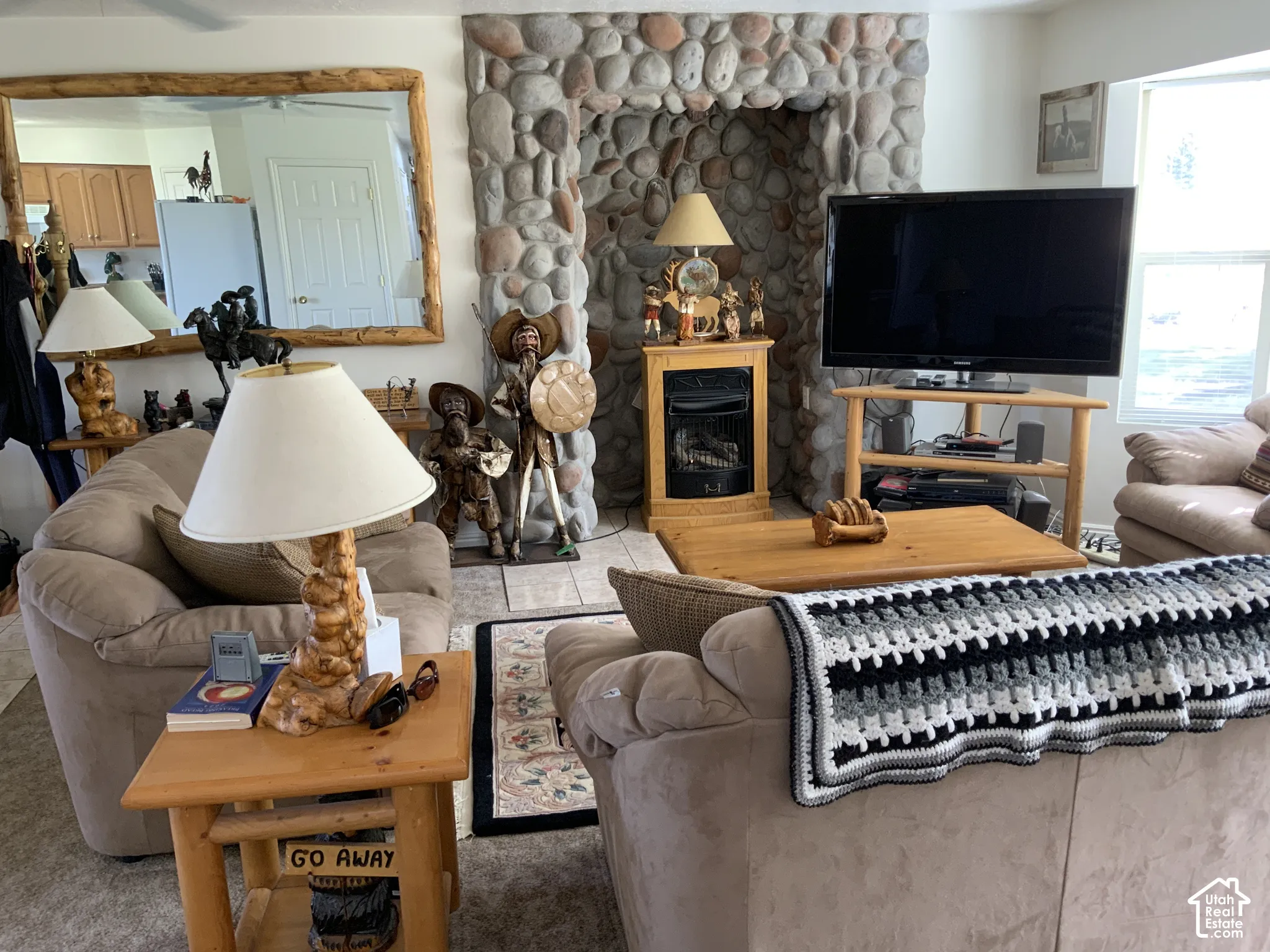 Stone-clad fireplace with built-in hearth, tiled flooring, ceiling fan, and large wall-mounted mirror