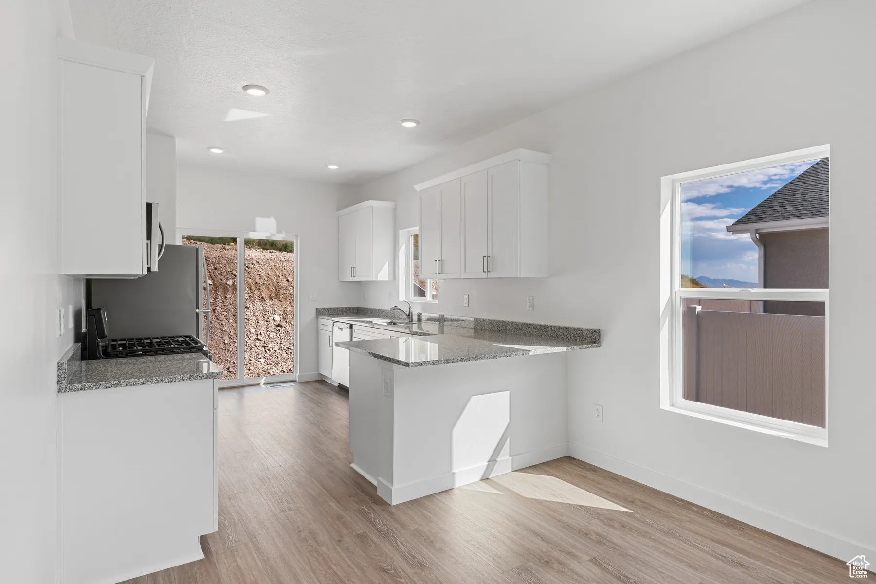 Kitchen with light stone countertops, white cabinetry, a peninsula, light wood-type flooring, and recessed lighting