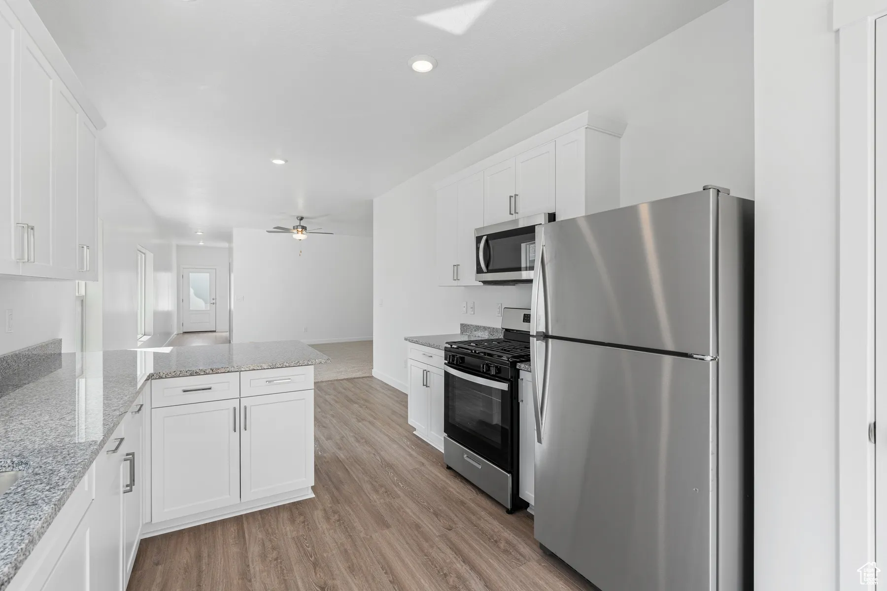 Kitchen featuring stainless steel appliances, white cabinetry, light stone countertops, a peninsula, and light wood finished floors