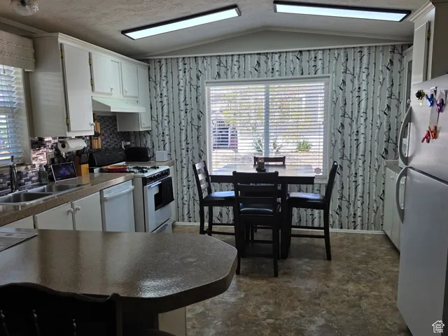 Kitchen featuring white appliances, vaulted ceiling, white cabinetry, dark countertops, and under cabinet range hood