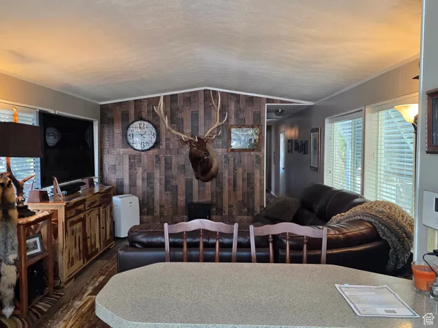 Living area featuring healthy amount of natural light, wood walls, vaulted ceiling, dark wood-type flooring, and a textured ceiling