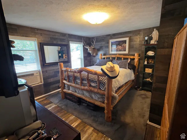 Bedroom featuring a textured ceiling, dark wood-style floors, and wooden walls