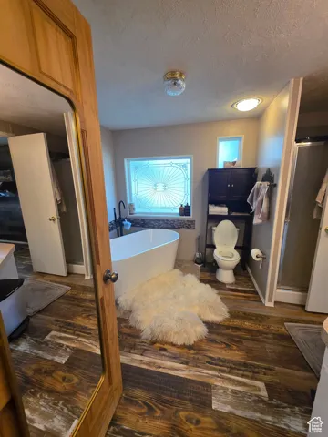 Bathroom featuring dark wood finished floors, a soaking tub, a textured ceiling, and a shower stall