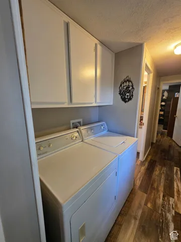 Laundry room with dark wood-style floors, a textured ceiling, separate washer and dryer, and cabinet space