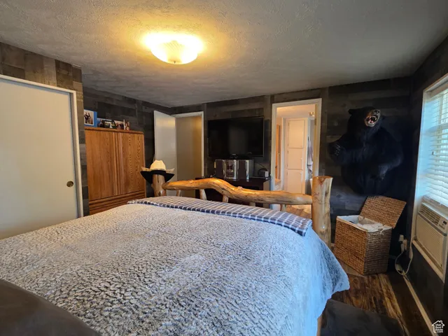 Bedroom with wooden walls, a textured ceiling, wood finished floors, cooling unit, and a closet