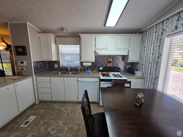 Kitchen with white appliances, backsplash, white cabinets, light countertops, and a textured ceiling
