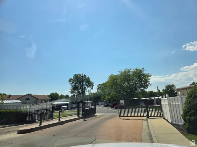 View of concrete road featuring a gate, sidewalks, a gated entry, and curbs