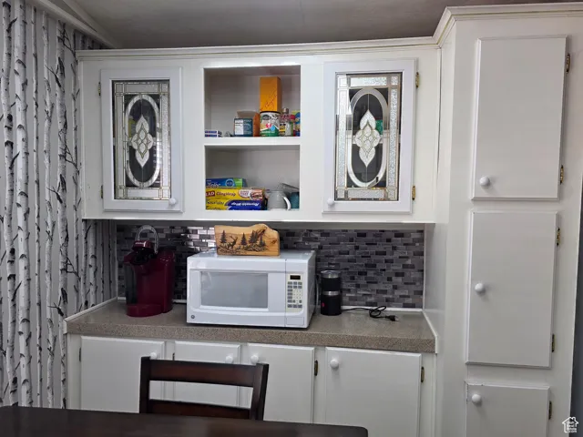 Bar area featuring white cabinetry, white microwave, light countertops, backsplash, and open shelves