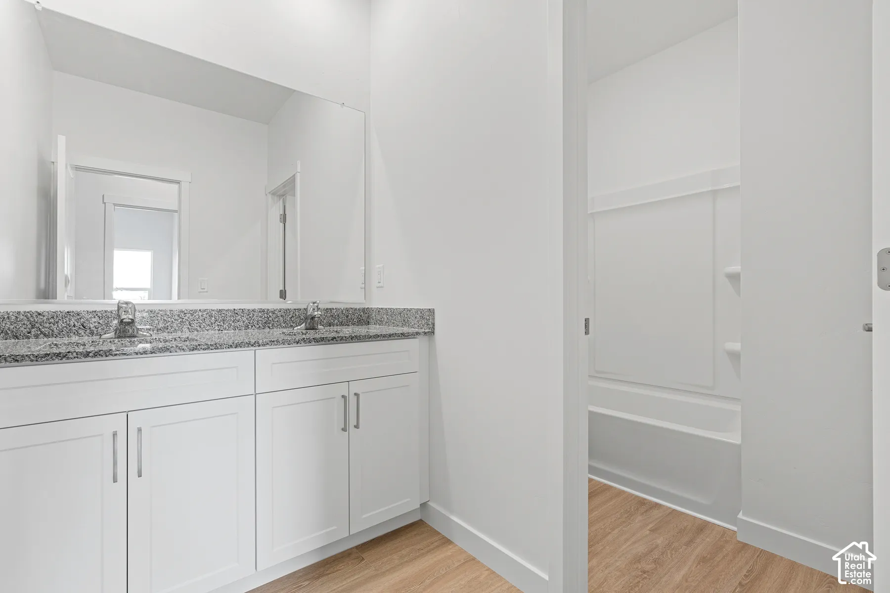 Bathroom with double vanity, light wood finished floors, and bathtub / shower combination