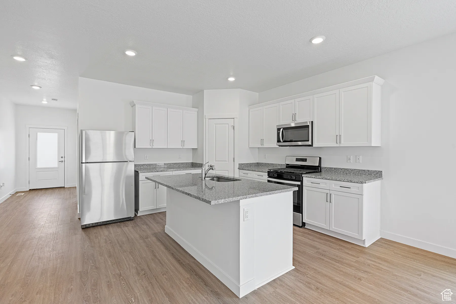 Kitchen with appliances with stainless steel finishes, white cabinets, light stone countertops, light wood-type flooring, and recessed lighting
