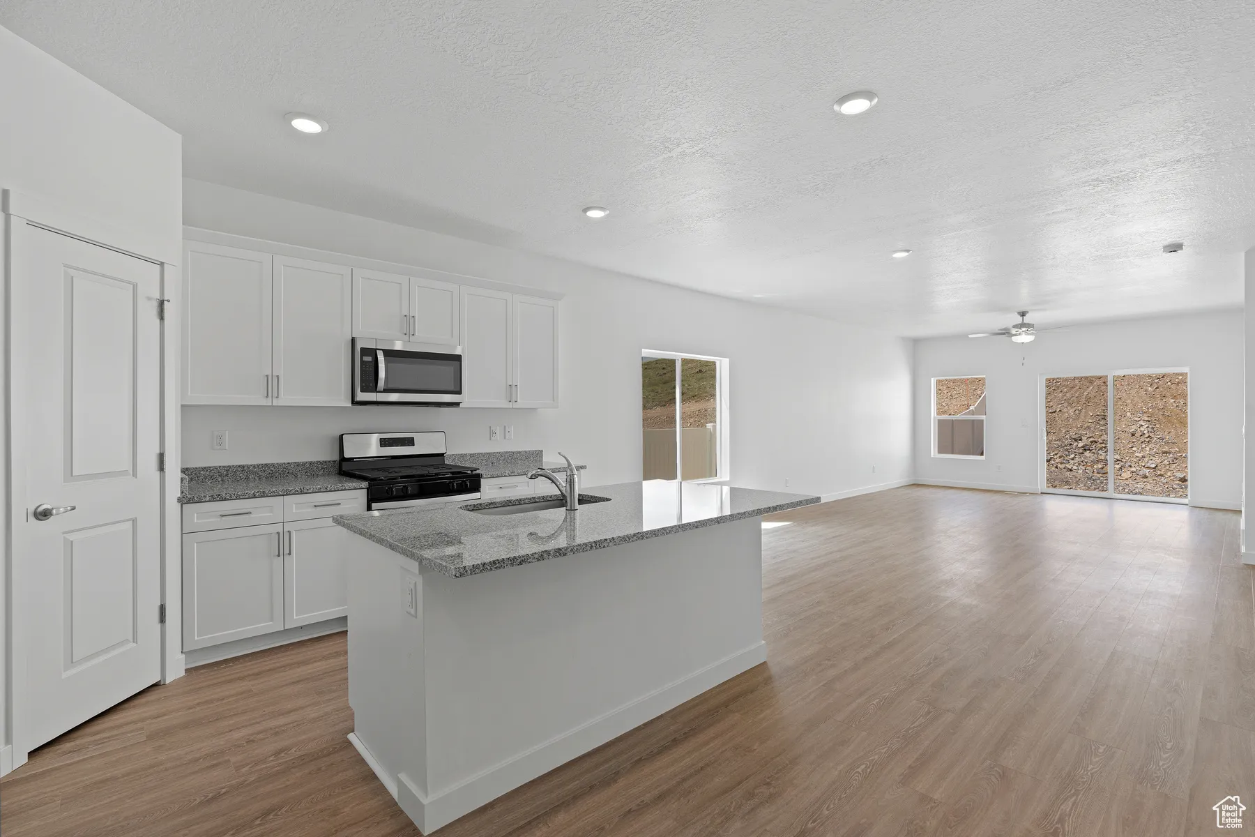 Kitchen with light stone counters, white cabinetry, appliances with stainless steel finishes, a kitchen island with sink, and light wood-style floors