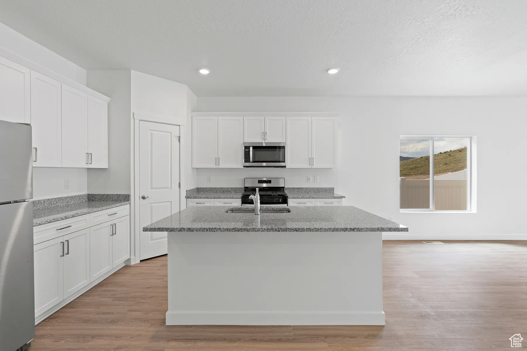 Kitchen with light stone countertops, white cabinetry, stainless steel appliances, light wood finished floors, and recessed lighting