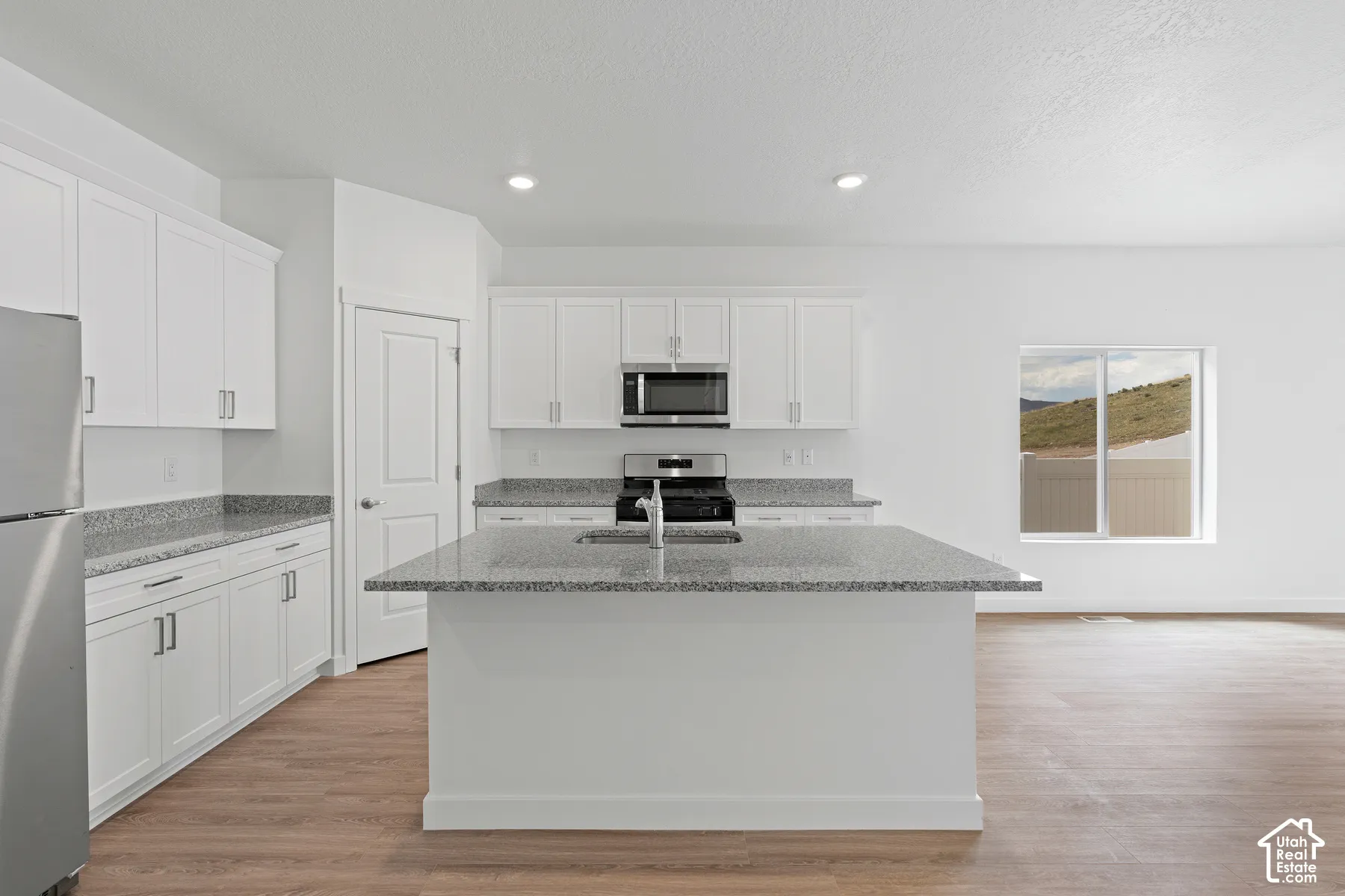 Kitchen with light stone countertops, white cabinetry, stainless steel appliances, light wood finished floors, and recessed lighting