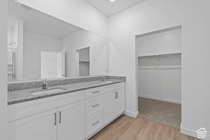 Bathroom featuring light wood-style flooring, a spacious closet, and double vanity
