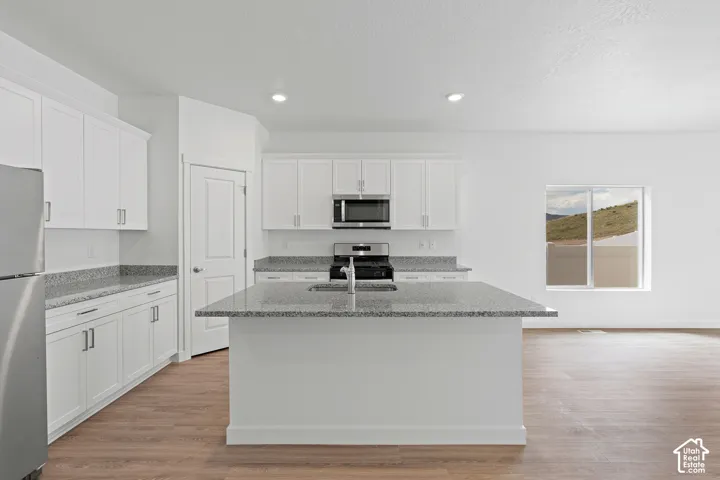 Kitchen with light stone countertops, white cabinetry, stainless steel appliances, light wood finished floors, and recessed lighting