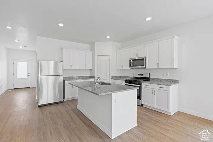 Kitchen with appliances with stainless steel finishes, white cabinets, light stone countertops, light wood-type flooring, and recessed lighting