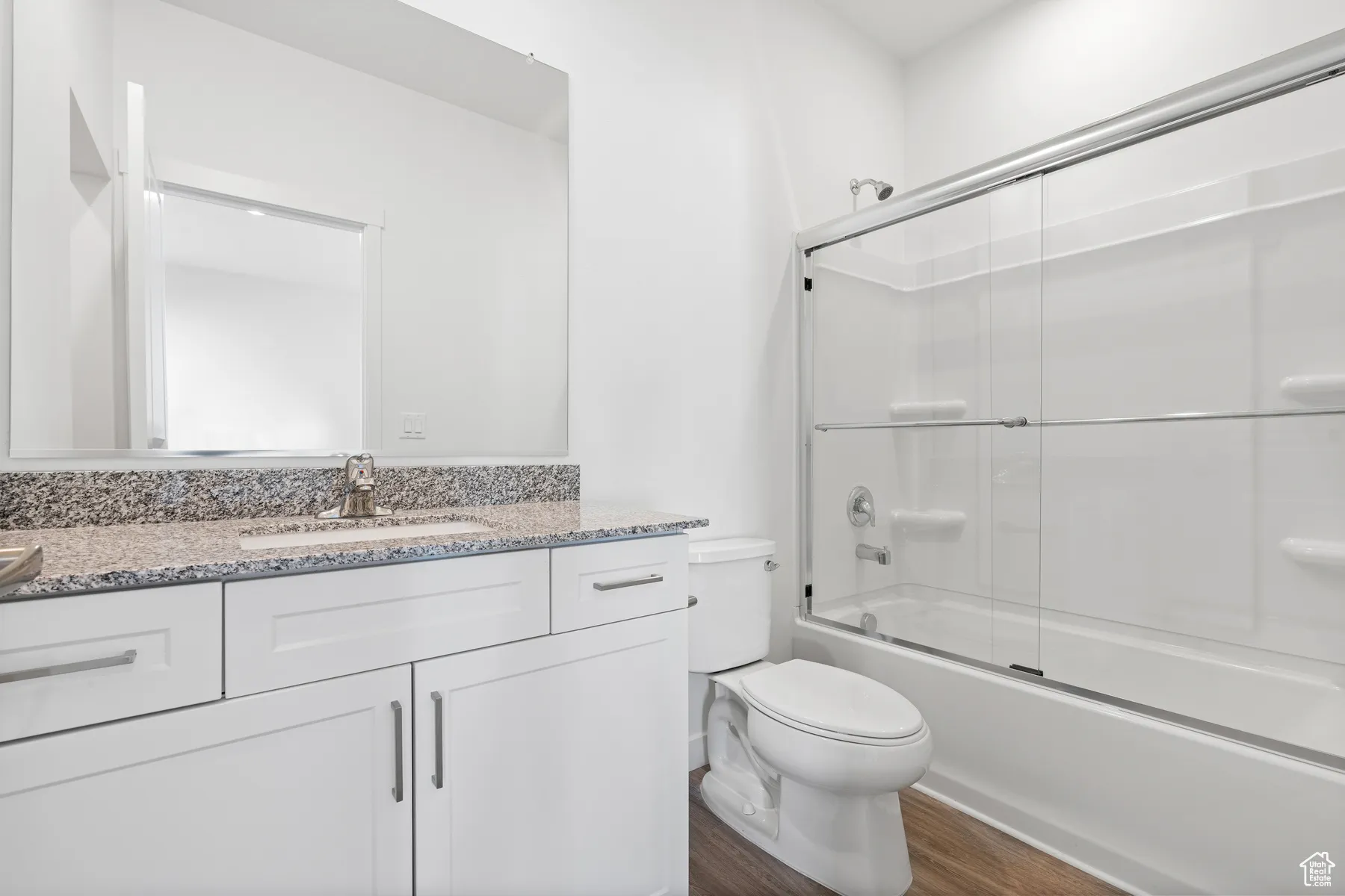 Full bathroom with enclosed tub / shower combo, vanity, and dark wood-type flooring