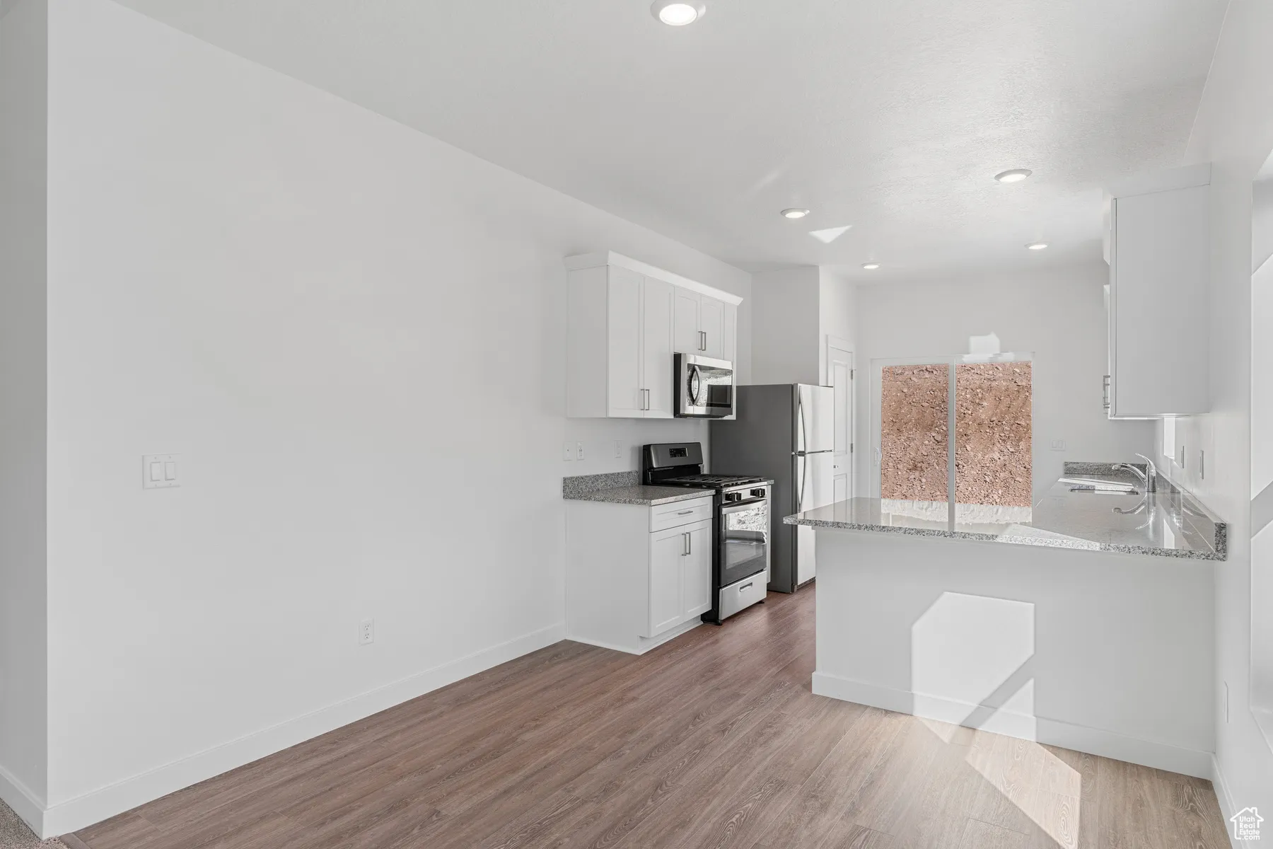 Kitchen featuring white cabinetry, light stone countertops, appliances with stainless steel finishes, a peninsula, and light wood-style flooring