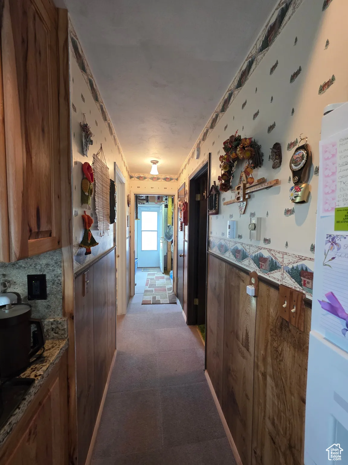 Kitchen featuring dark colored carpet, freestanding refrigerator, brown cabinets, dark stone counters, and wallpapered walls