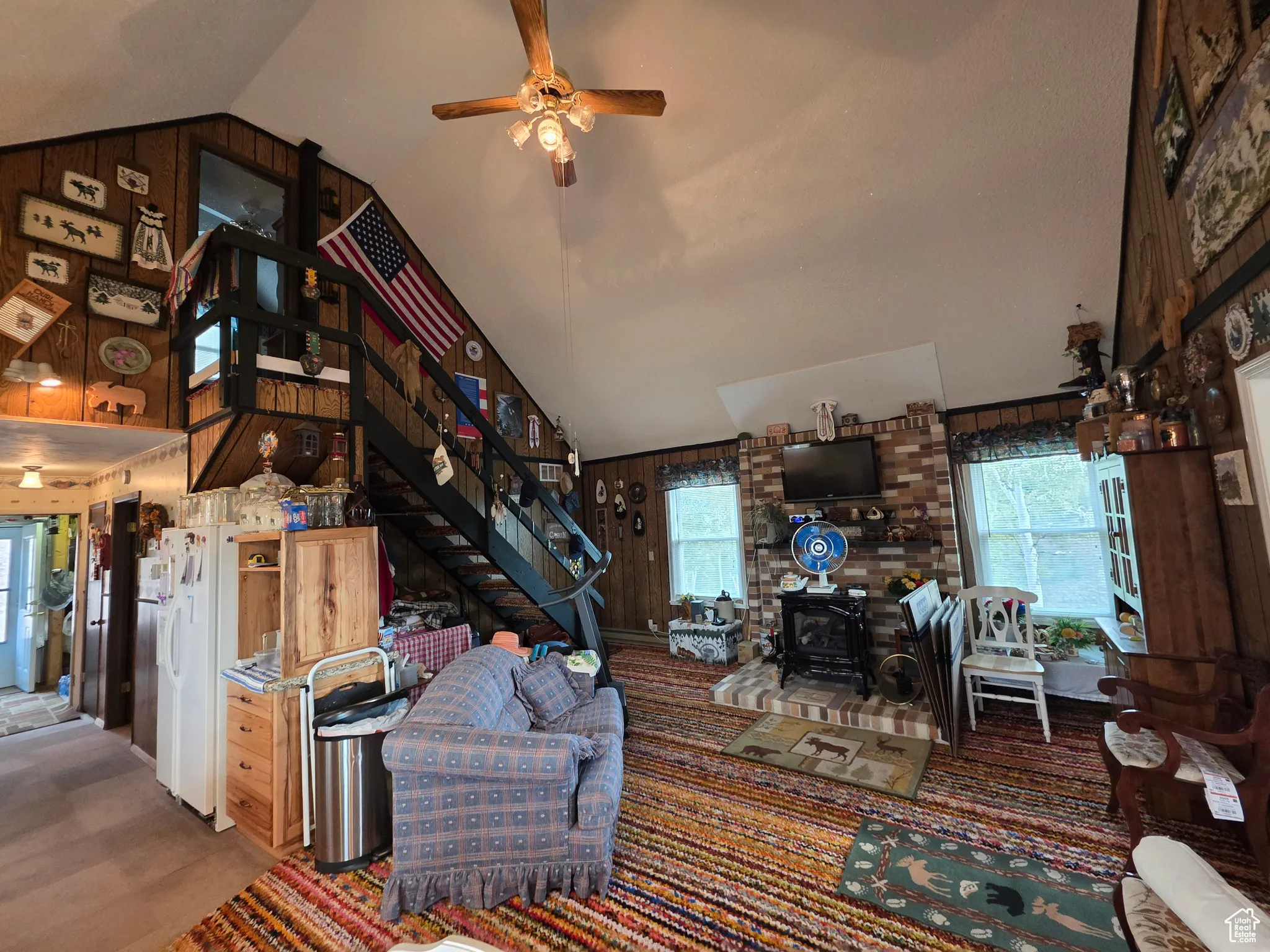 Living area featuring wood walls, plenty of natural light, a wood stove, stairs, and high vaulted ceiling