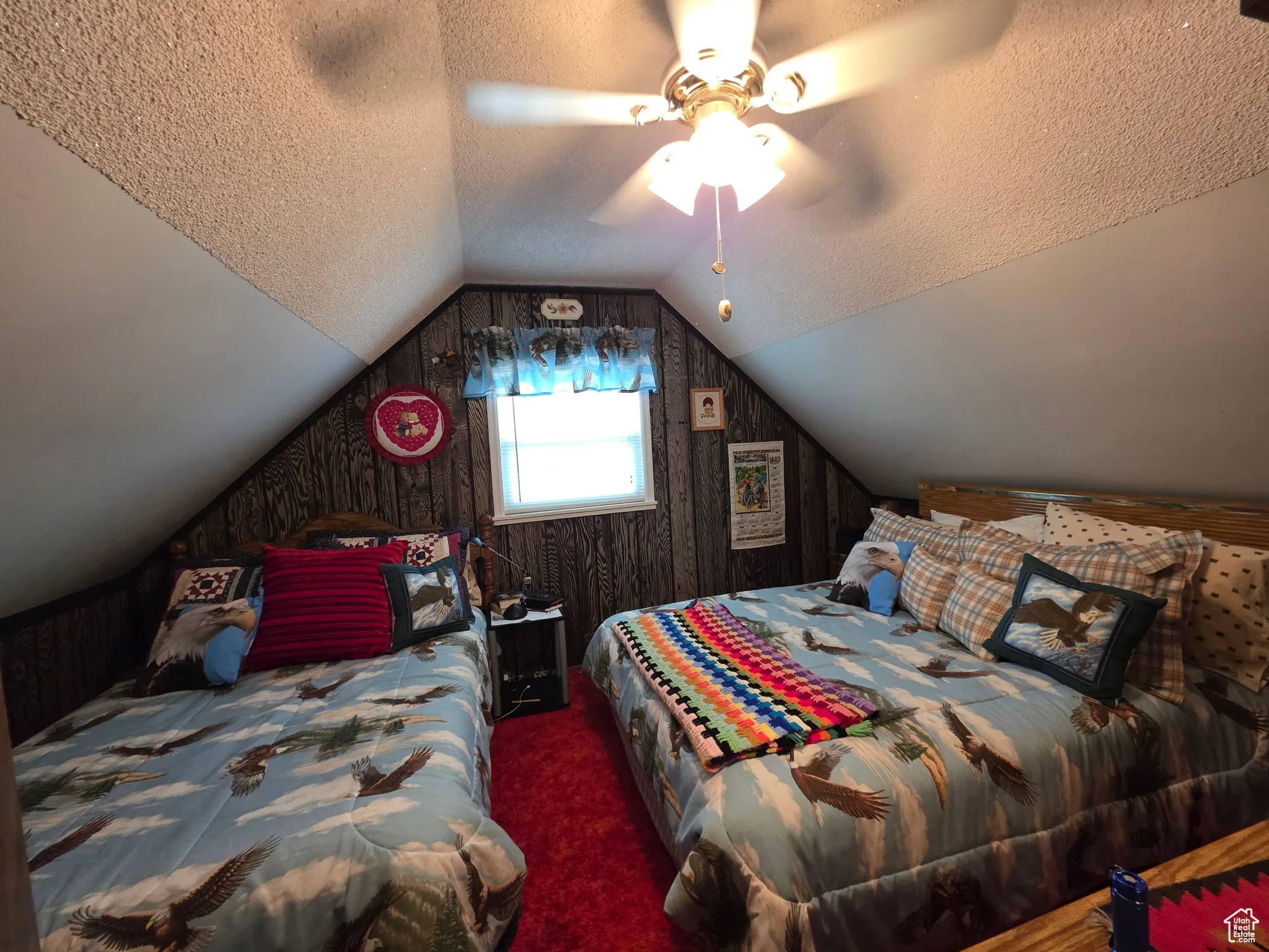 Carpeted bedroom with a textured ceiling, wood walls, lofted ceiling, and a ceiling fan