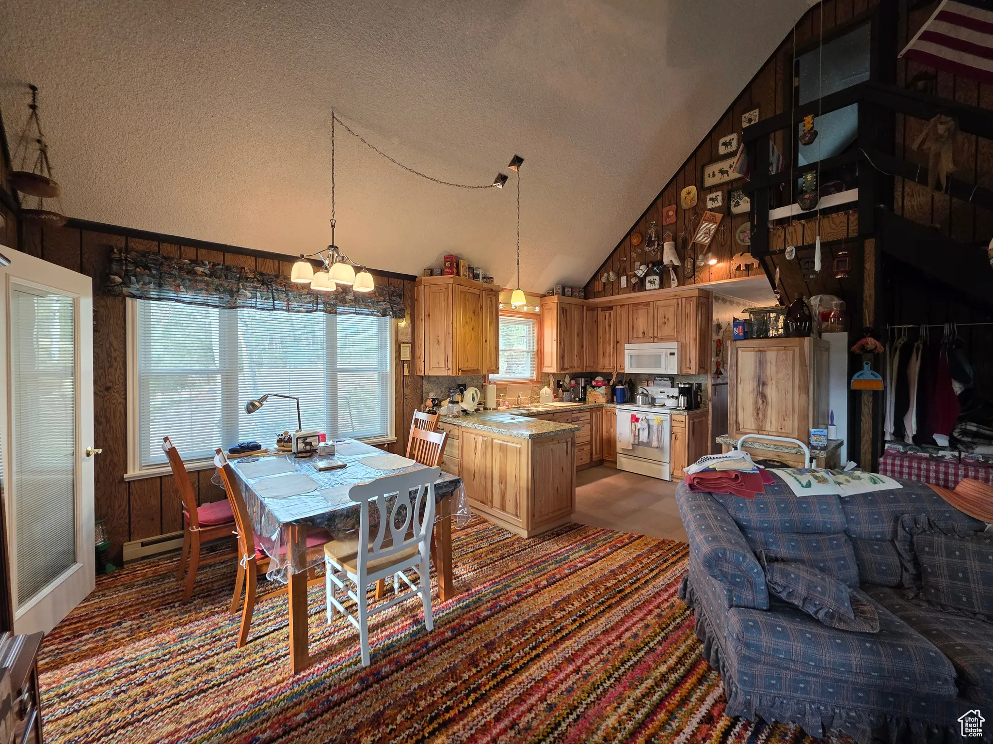 Dining area featuring a textured ceiling, high vaulted ceiling, a chandelier, wood walls, and a baseboard heating unit