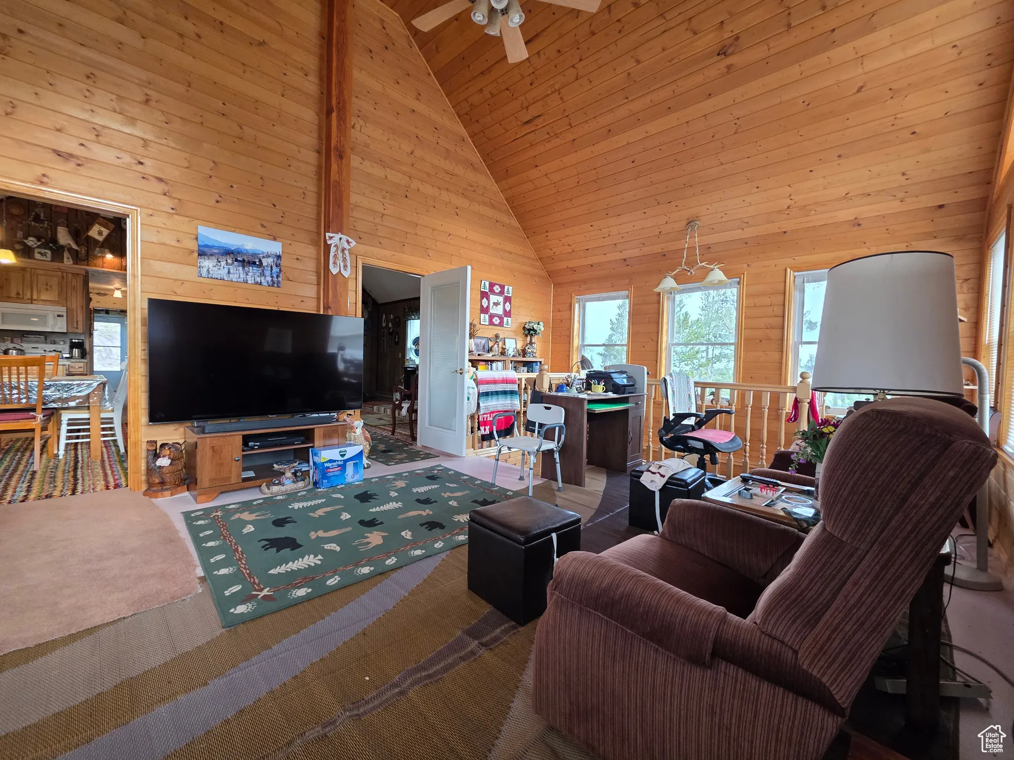 Carpeted living room featuring wood walls, high vaulted ceiling, wood ceiling, and a ceiling fan