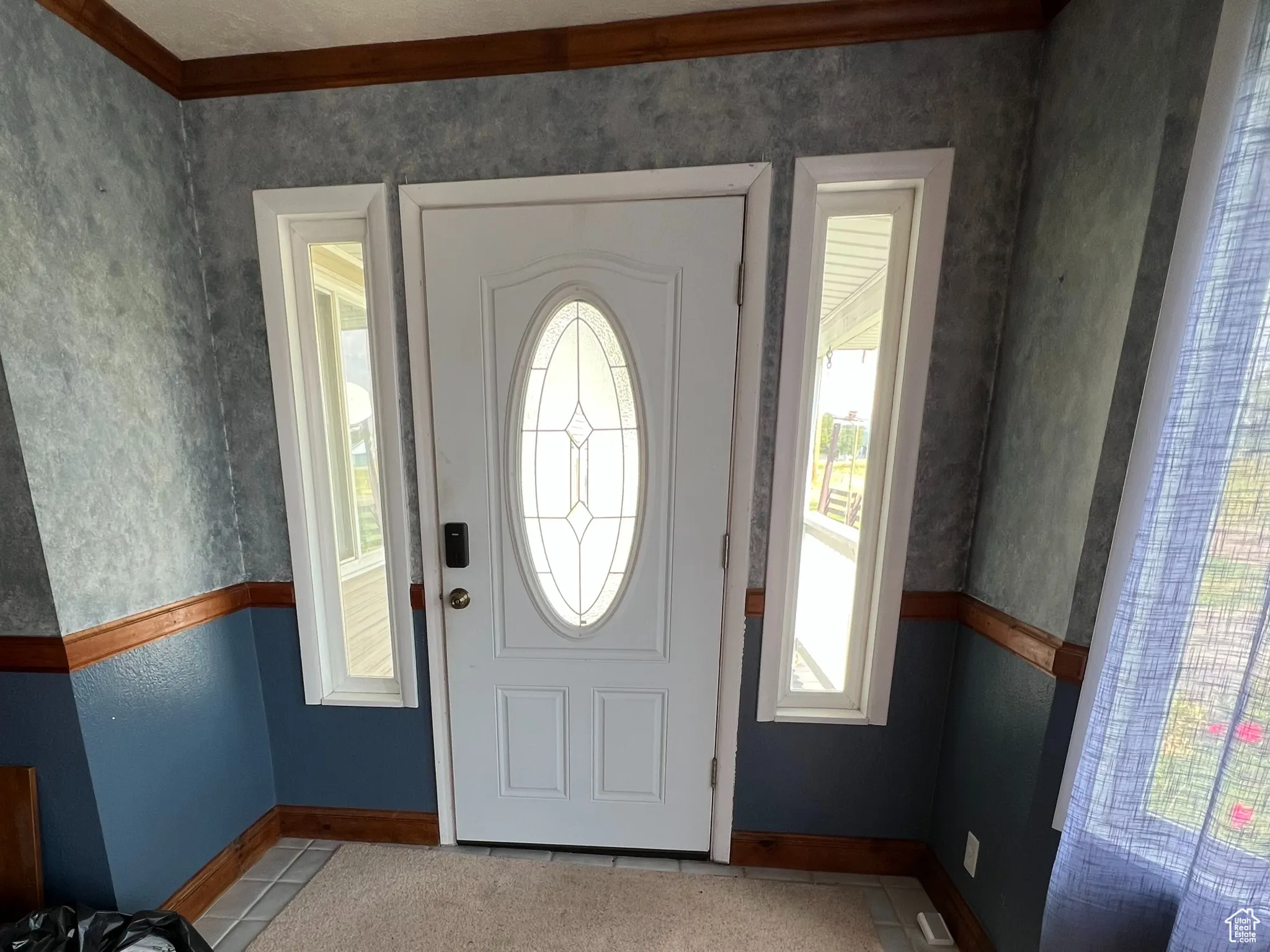 Entryway with a textured ceiling, light wood-style flooring, crown molding, wallpapered walls, and a wainscoted wall