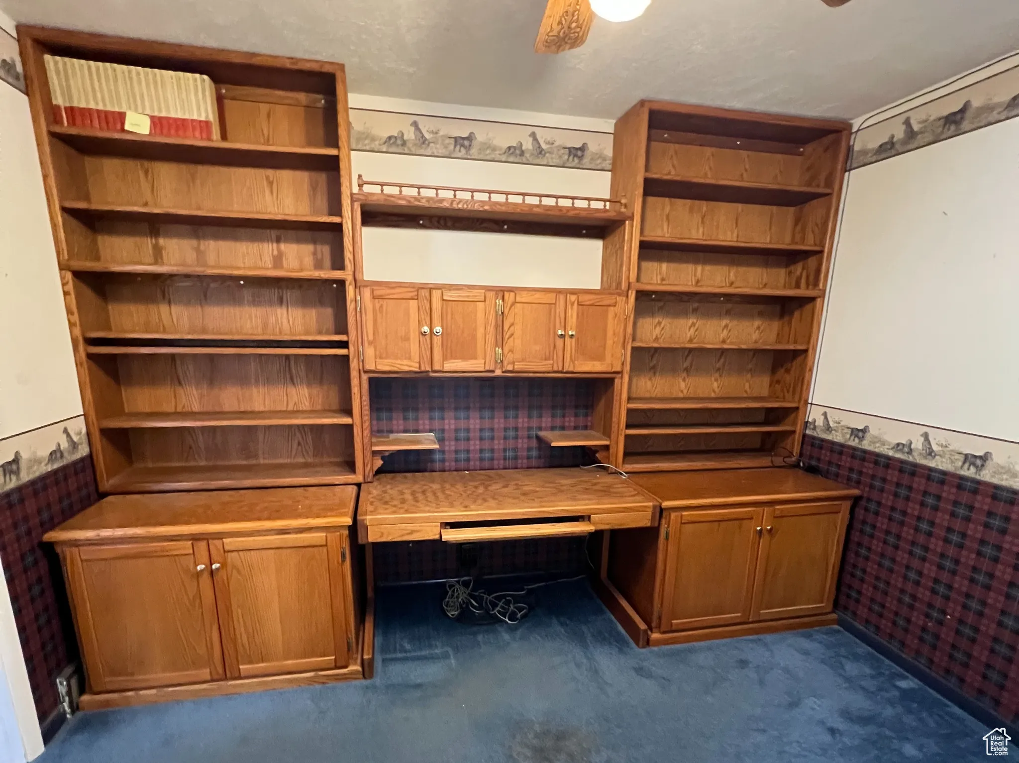Unfurnished office with a wainscoted wall, wallpapered walls, dark carpet, and a ceiling fan