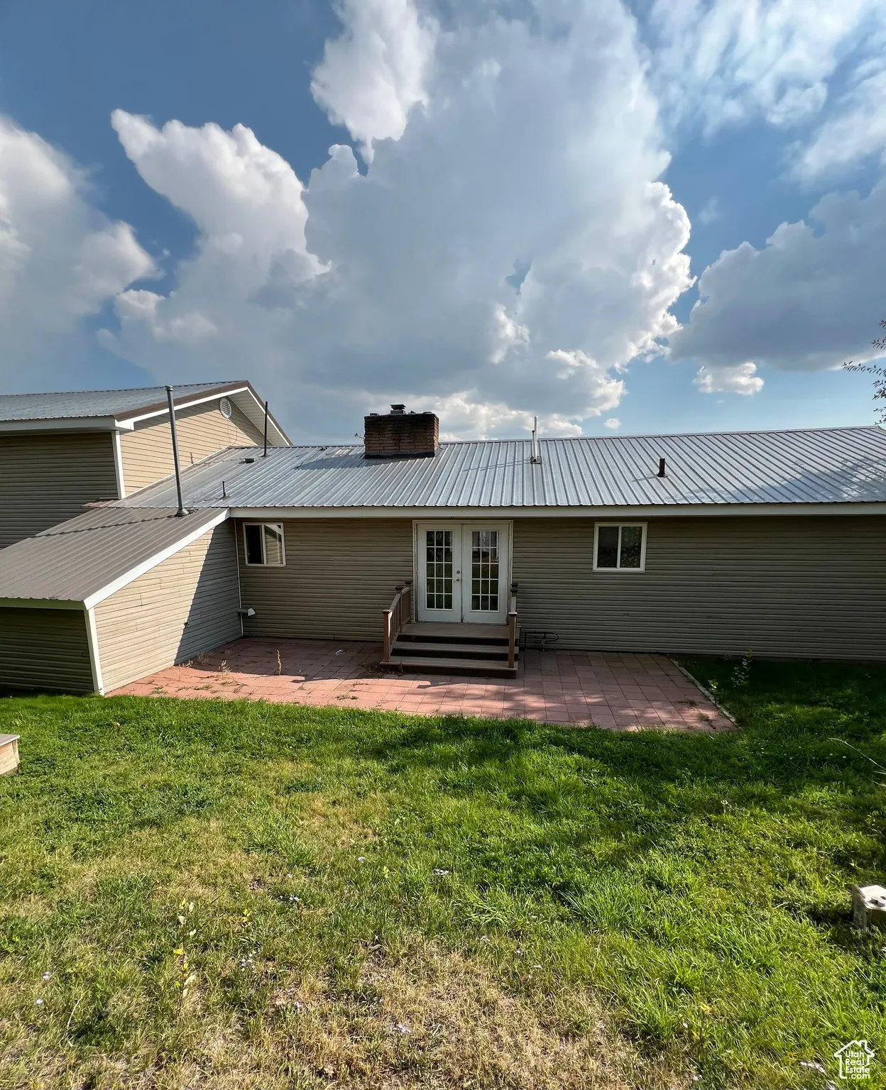 Back of property featuring a patio, a metal roof, a chimney, a yard, and french doors