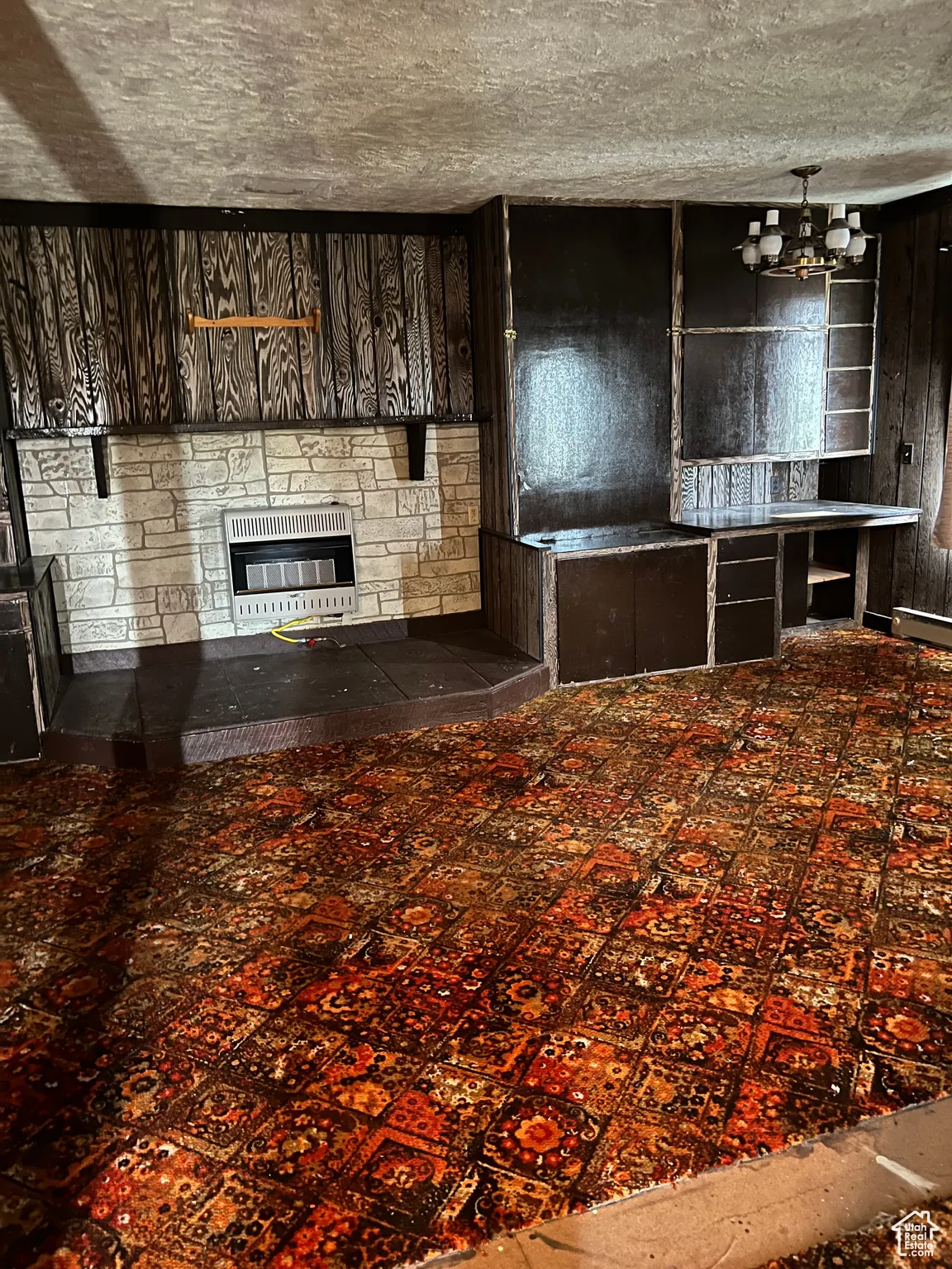 Unfurnished living room featuring heating unit, a chandelier, and a stone fireplace