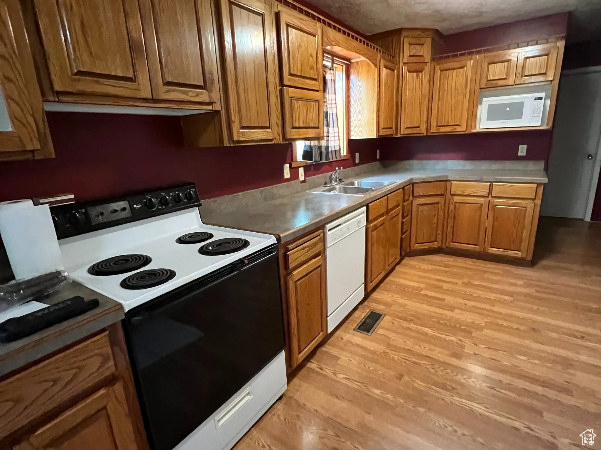 Kitchen featuring brown cabinetry, white appliances, light wood-style floors, and a textured ceiling