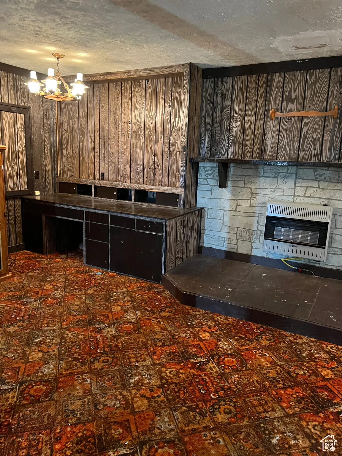 Kitchen featuring heating unit, a glass covered fireplace, wood walls, and a chandelier