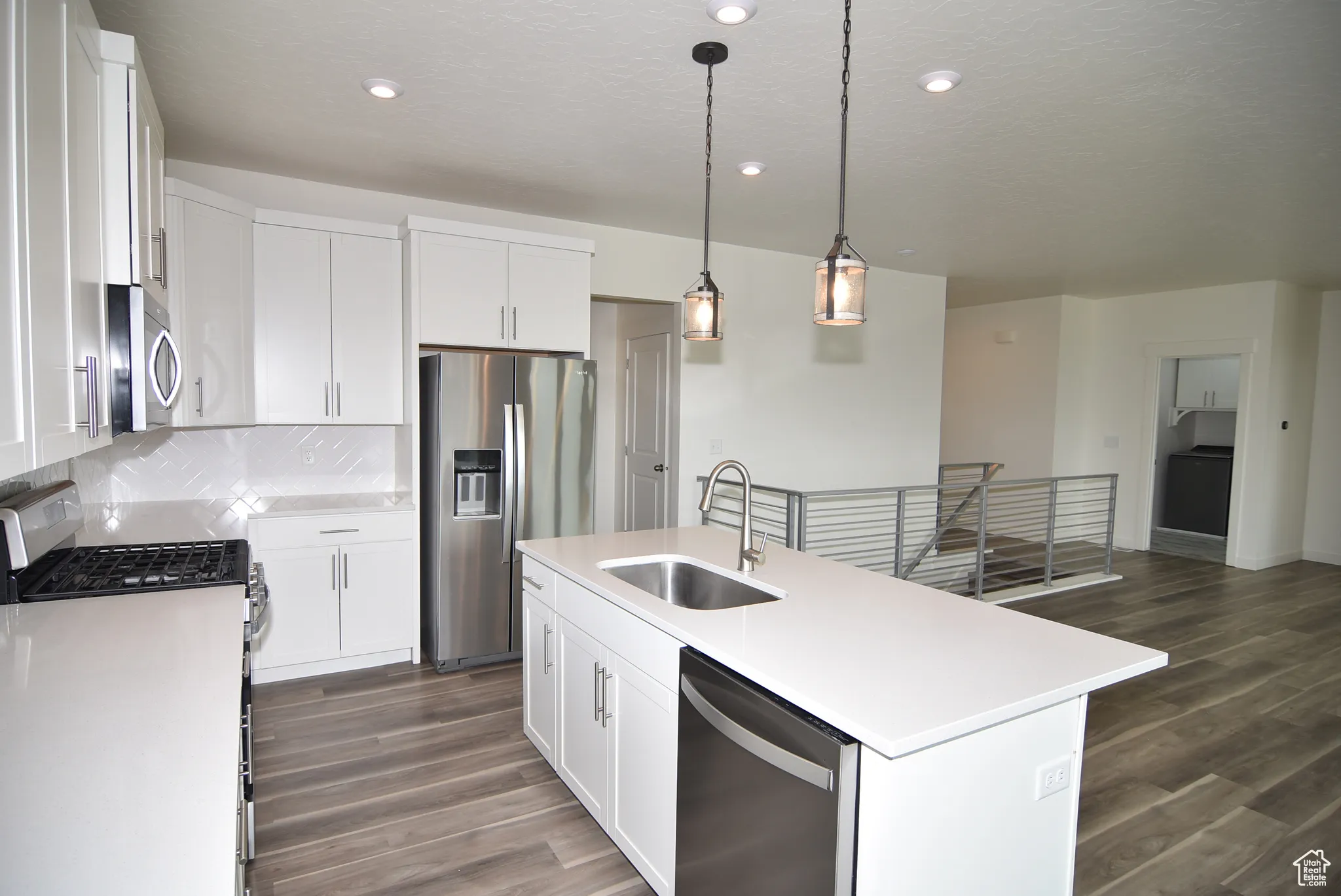 Kitchen with appliances with stainless steel finishes, pendant lighting, white cabinets, dark wood-style floors, and a textured ceiling