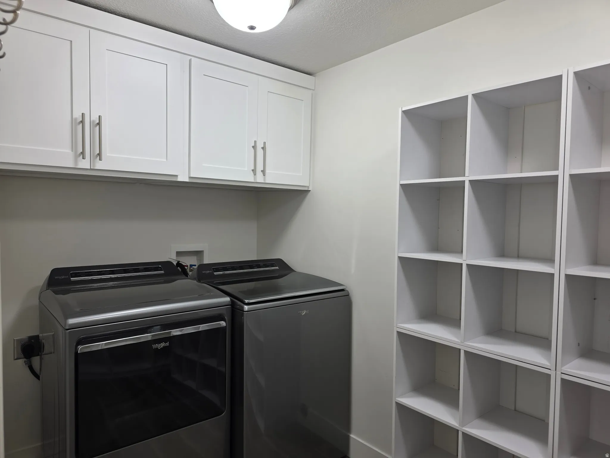 Laundry area featuring separate washer and dryer, a textured ceiling, and cabinet space
