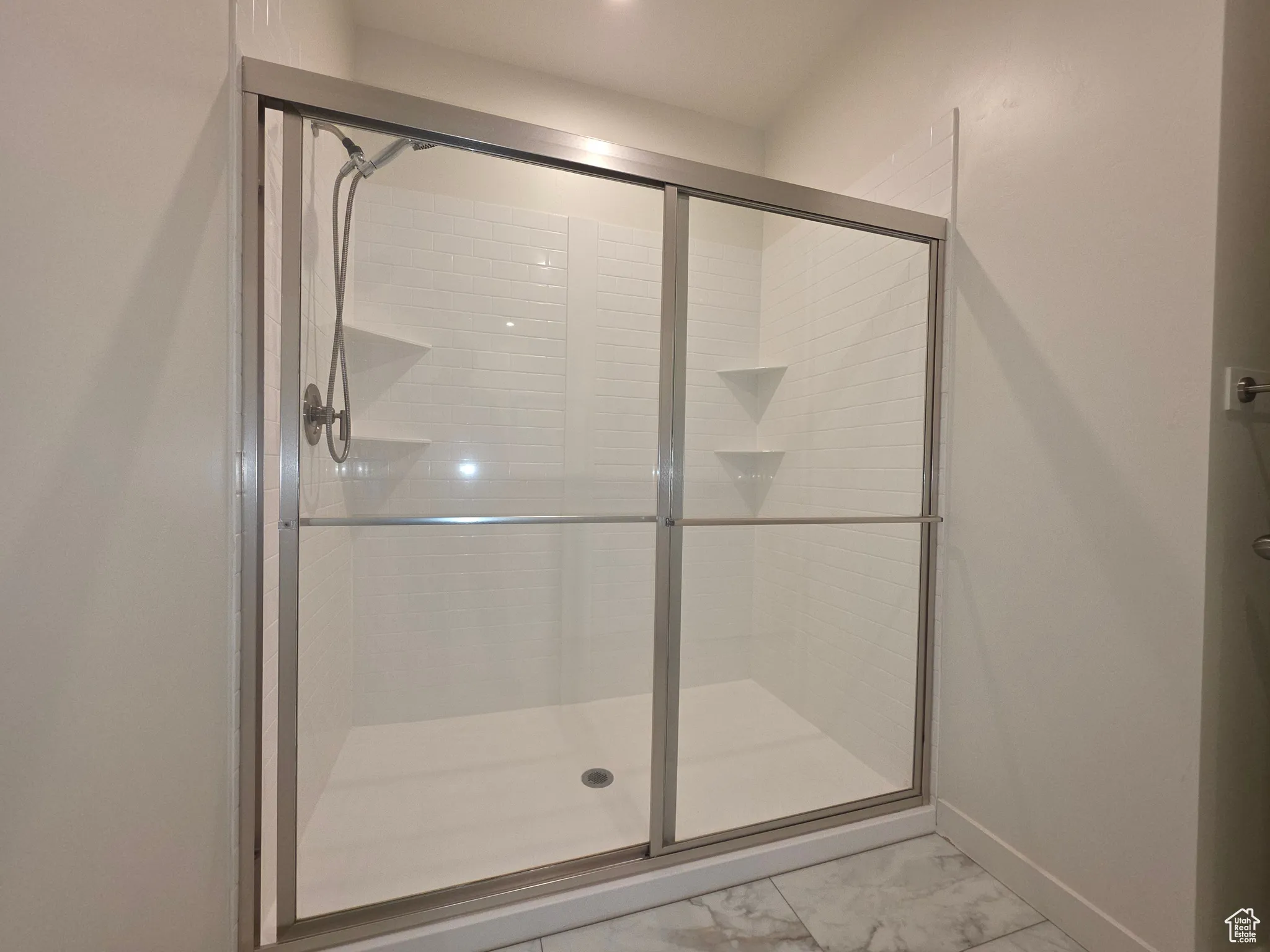 Full bath with a shower stall and light marble finish flooring