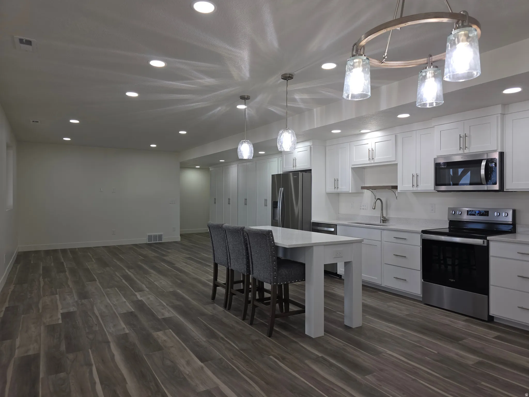 Kitchen with appliances with stainless steel finishes, white cabinets, recessed lighting, hanging light fixtures, and dark wood finished floors