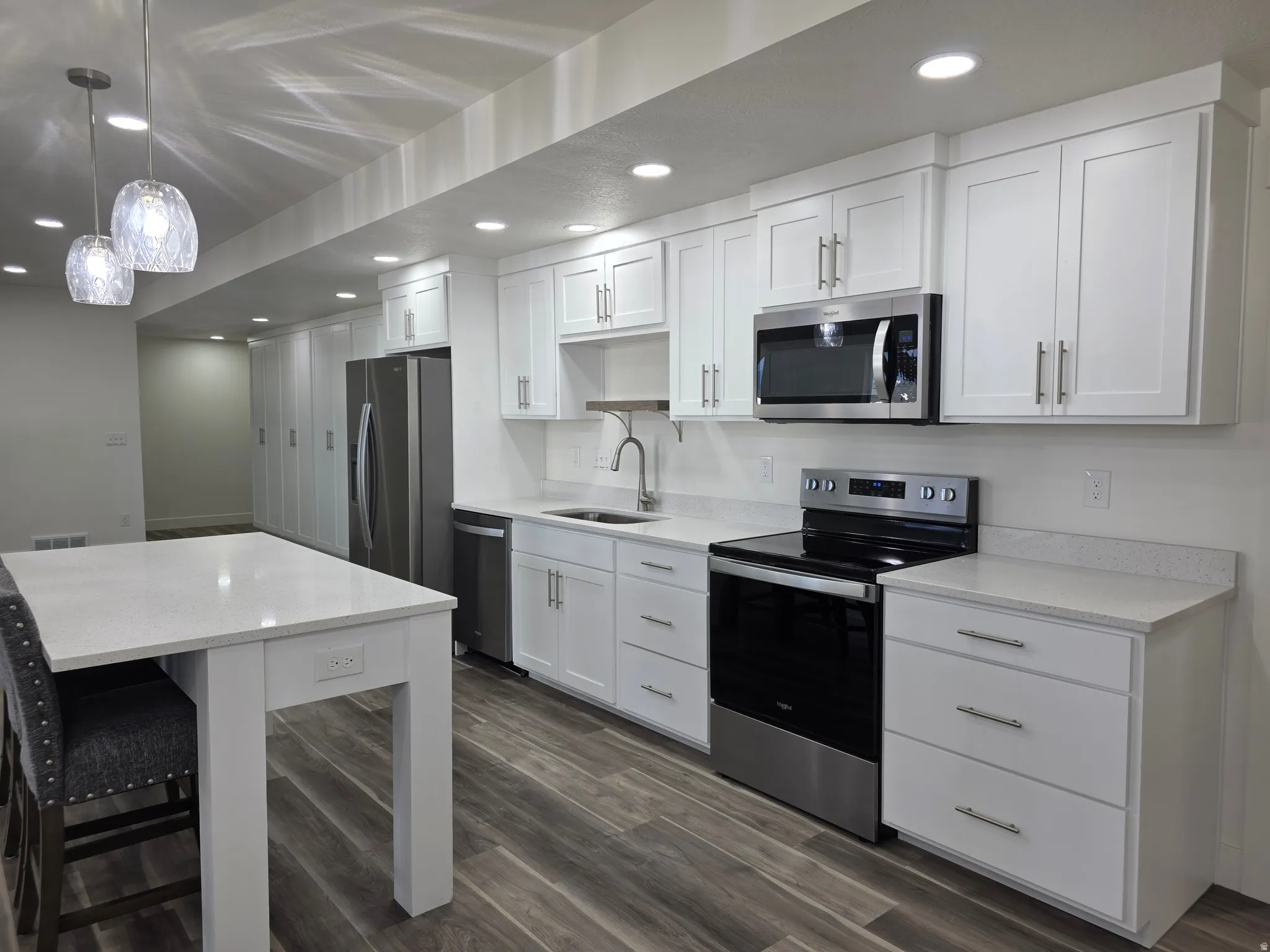 Kitchen with appliances with stainless steel finishes, white cabinetry, pendant lighting, light stone countertops, and recessed lighting