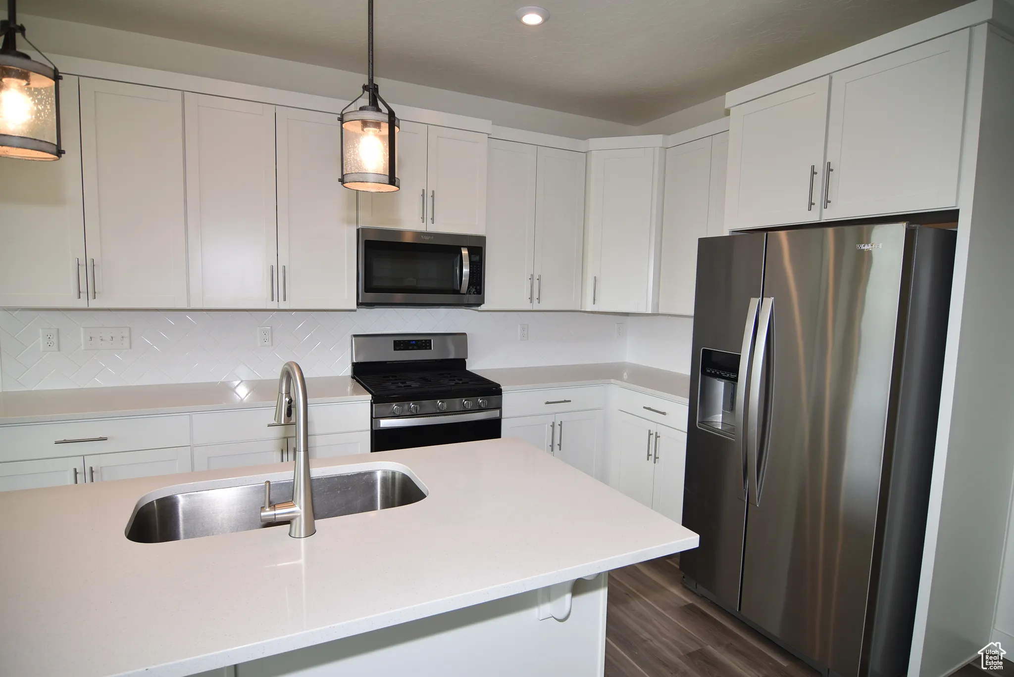 Kitchen with stainless steel appliances, white cabinetry, quartz counter tops decorative light fixtures, recessed lighting and quarts counter tops