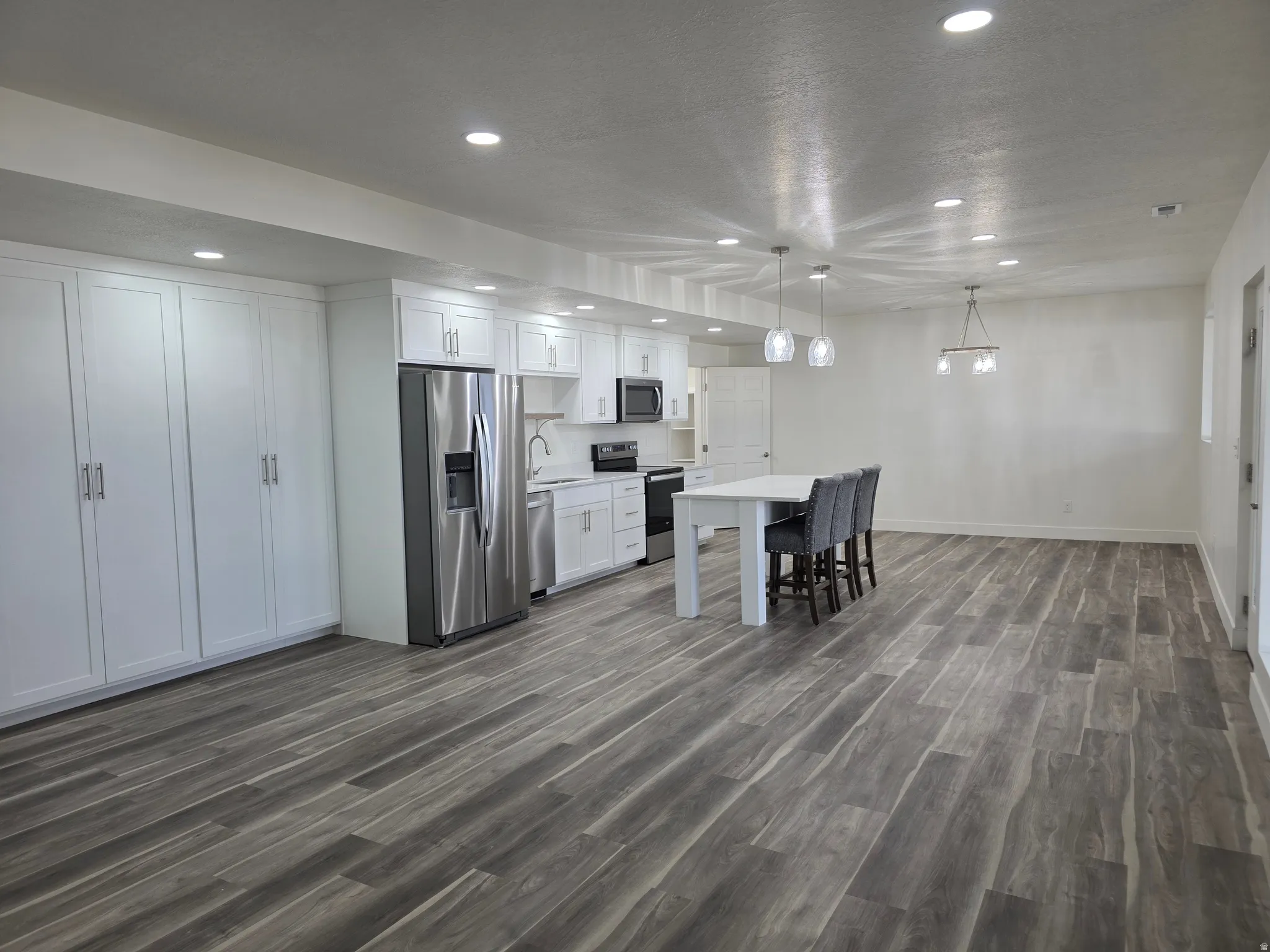Kitchen with white cabinetry, appliances with stainless steel finishes, dark wood-type flooring, recessed lighting, and pendant lighting