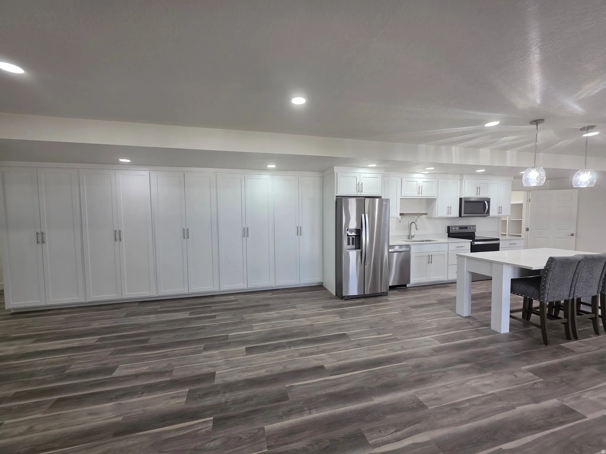 Kitchen featuring white cabinetry, stainless steel appliances, pendant lighting, dark wood-type flooring, and a kitchen breakfast bar