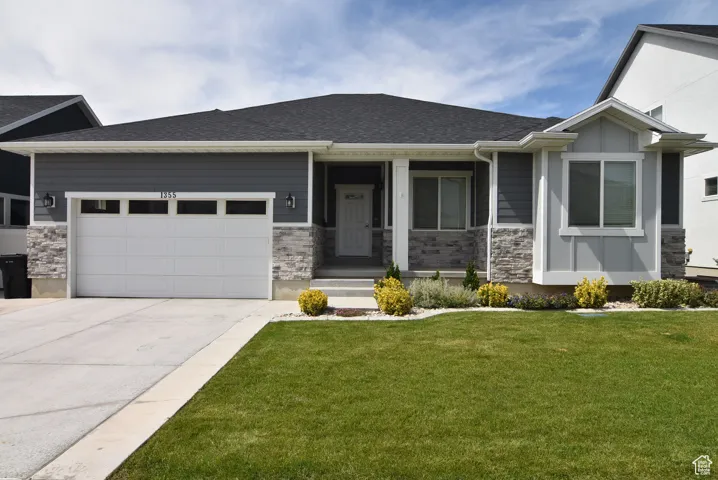 View of front of property with stone siding, roof with shingles, a front lawn, concrete driveway, and an attached garage