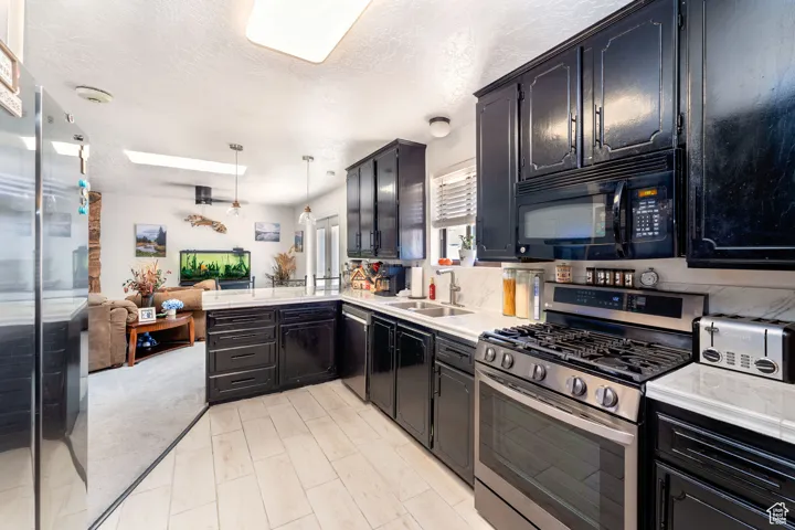 Kitchen with stainless steel appliances, a textured ceiling, dark cabinets, open floor plan, and a peninsula