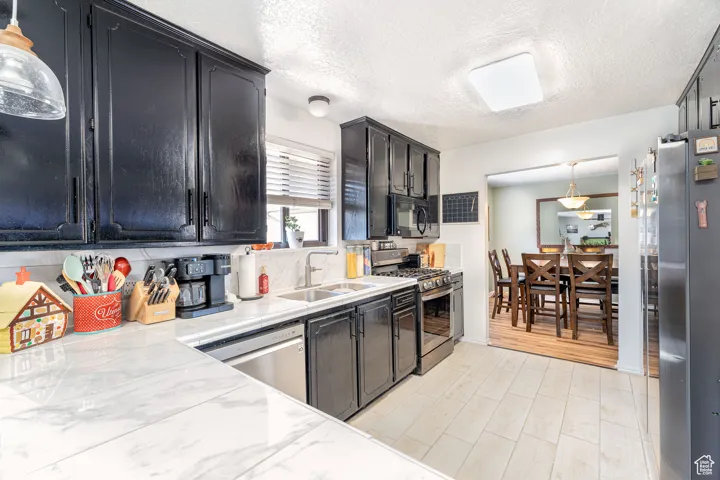 Kitchen with pendant lighting, dark cabinetry, appliances with stainless steel finishes, light countertops, and a textured ceiling