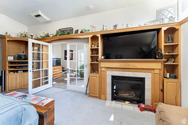Carpeted living area featuring french doors, a tiled fireplace, and a textured ceiling
