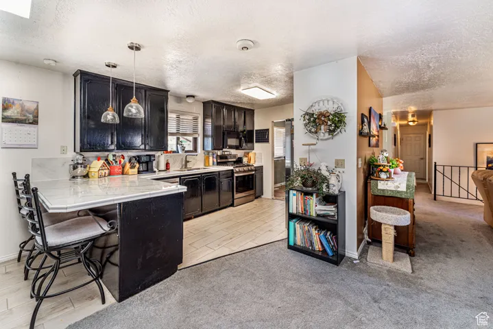 Kitchen featuring a textured ceiling, a breakfast bar area, a peninsula, dark cabinets, and stainless steel gas range oven