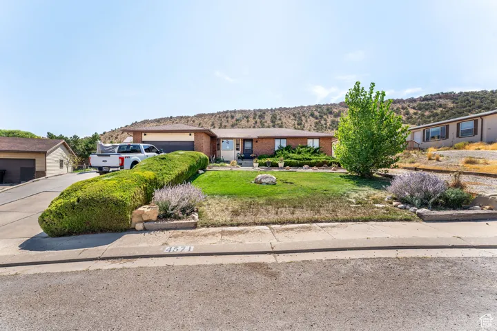 View of front of home with driveway, a front yard, brick siding, an attached garage, and a mountain view